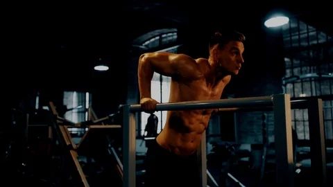 Man doing triceps dip exercise on bars in dark gym Stock Footage 99038247