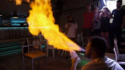 Man doing trick spraying vodka flame from bottle sets on fire stack of glasse Stock Footage 81259791