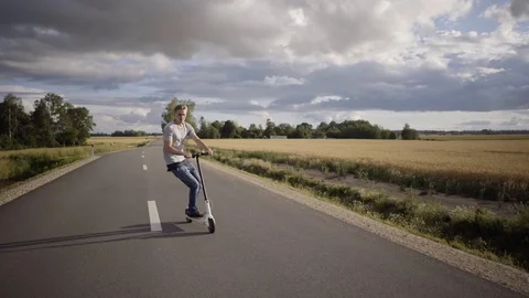 Man doing tricks with an electric scooter on the road . Blue skies with Stock Footage 114763297