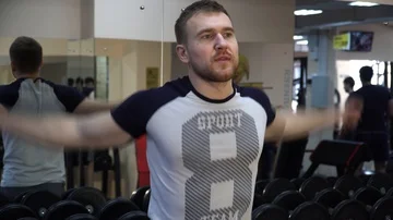 Man doing warm-up in the gym, against a background of dumbbells Stock Footage 85953367