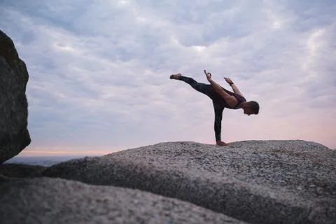 Man doing the warrior three pose on rocks at dusk Stock Photos