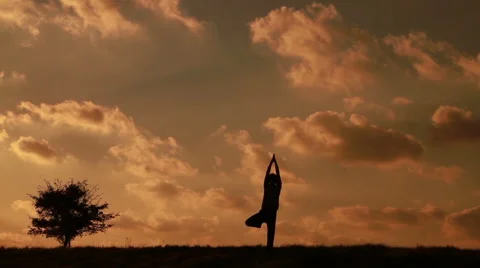 Man doing yoga asanas on a background of clouds and near the small tree Stock Footage 67652206