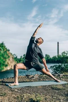 Man doing yoga exercise on the quarry lake at sunny day. International Day of Stock Photos