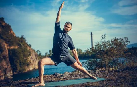 Man doing yoga exercise on the quarry lake at sunny day. International Day of Stock Photos