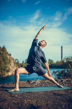Man doing yoga exercise on the quarry lake at sunny day. International Day of Stock Photos