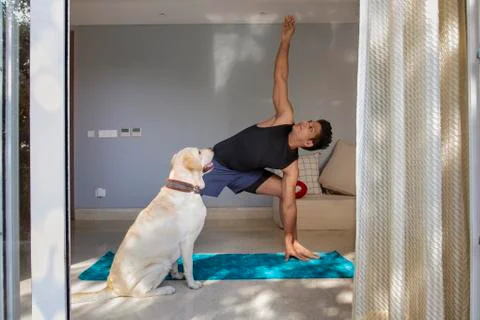 Man doing yoga exercises while his dog watches him.  Stock Photos