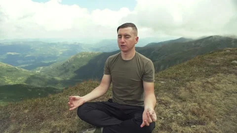 Man is doing yoga in the mountains, doing the exercise Lotus position on the top Stock Footage 218438977