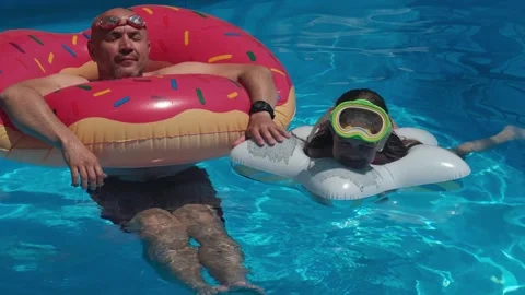 Man in donut float and girl in diving mask swimming in pool 動画素材 338282691