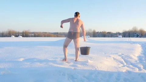 Man douses himself with cold water from a bucket while standing in the snow Vidéo 146520834