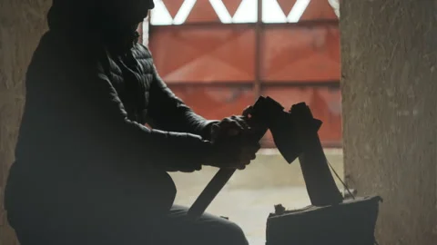 Man in the down jacket is chopping wood, in silhouette view  in a barn environme Stock Footage 257060823