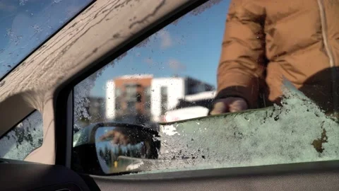A man in down jacket cleans ice from the side window of a car Stock Footage 164865154