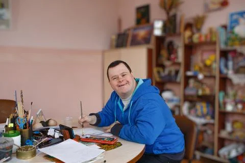 A man with down syndrome is engaged in drawing in a workshop. Stock Photos