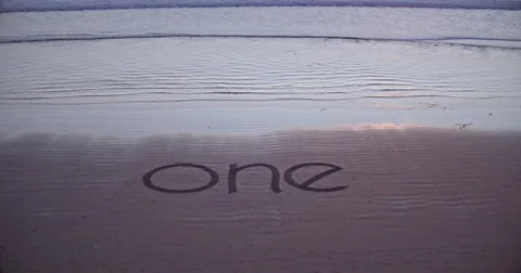 Man drawing a design of the word one on the beach Stock Footage 58649743