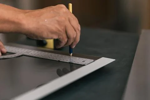 Man drawing a line using a square on a surface in a workshop. Stock Photos