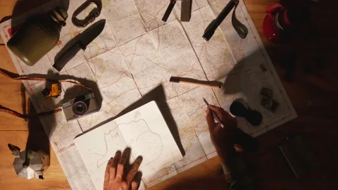 Man drawing map on his rustic table with camping accessories	 Stock Footage 163986068