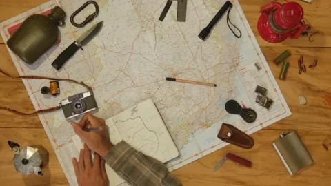 Man drawing map on his rustic table with camping accessories	 Stock Footage 163986077