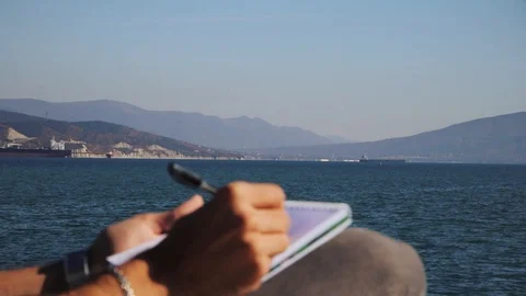 Man drawing in notebook in front of sea, In slow motion Stock Footage 118216393