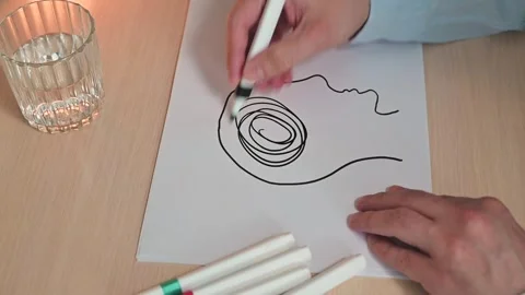 A man draws an abstract tangled line drawing of a person's head on a piece of 스톡 동영상 337558649
