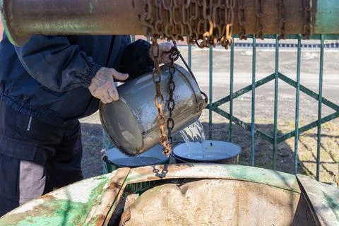 A man draws fresh water using a metal bucket and rusted chain from a Stock Photos