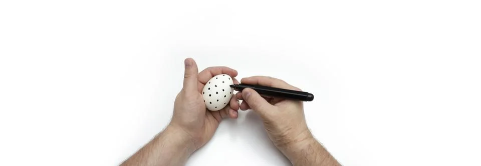 Man draws pattern of dots on eggshell with black marker 스톡 사진