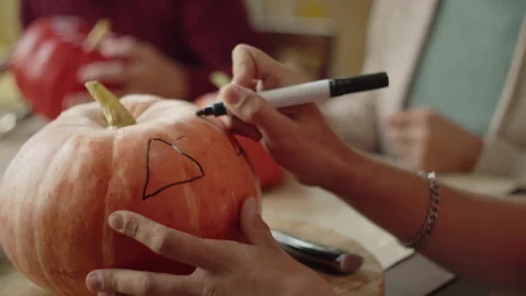 A man draws on a pumpkin with a marker and carefully examines the lamp Stock Footage 163254480