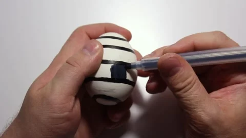 Μan draws striped pattern on eggshell of white chicken egg with black marker Stock Footage 270005918