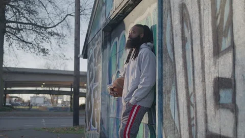 Man with Dreadlocks and Beard Holdds Basketball Under His Arm Outdoors at Sunset Stock Footage 270397384