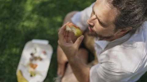 Man with dreadlocks eating apple at park picnic Stock Footage 319984870