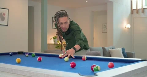 Man with dreadlocks entering home, chalking cue at pool table, aligning shot and Stock Footage 336305771