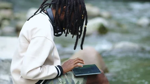 A Man With Dreadlocks Focusing on His Tablet in The Nature Stock Footage 209127481