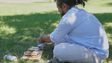 Man with dreadlocks preparing vegan burgers during picnic Stock Footage 321343388
