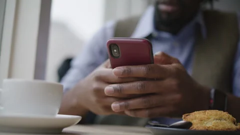 A man with dreadlocks sits in a cozy coffee shop, focused on his mobile phone Stock Footage 312578640