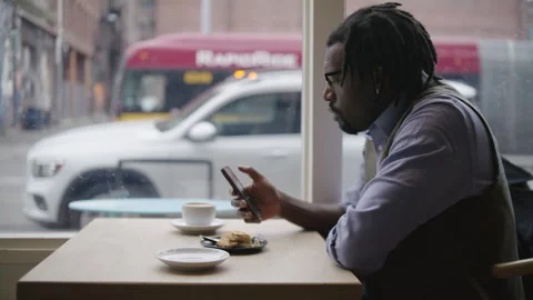 Man with dreadlocks uses mobile phone in coffee shop during rainy day Stock Footage 312578975