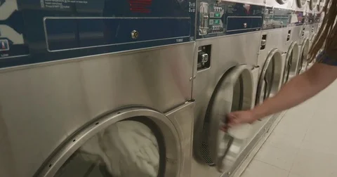 Man with Dreads putting Clothes into a Dryer at Laundromat Stock Footage 84154366