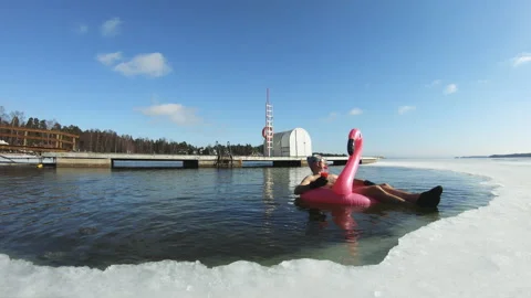 A man dreaming of a vacation floating on an inflatable flamingo in an ice hole Stock Footage 161036787
