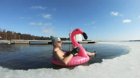 A man dreaming of a vacation floating on an inflatable flamingo in an ice hole Stock Footage 161047279