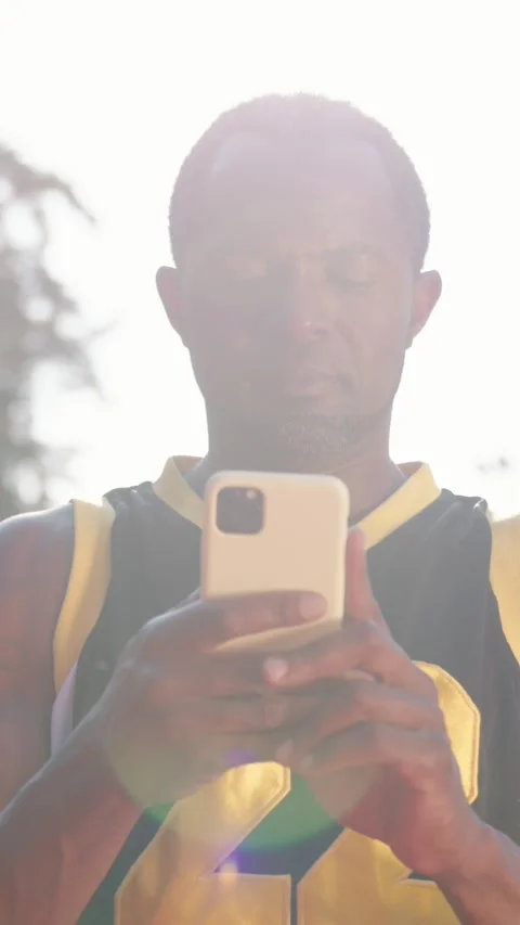 A man dressed in a basketball jersey is seen using his smartphone while outside Stock Footage 314209149