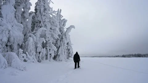 Man dressed in black colored snow gear is snowshoeing along the shore of lake Stock Footage 230920145