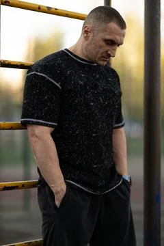 Man dressed in black workout clothes stands near playground structures lost in Stock Photos