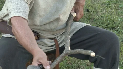 A man dressed in medieval clothes carving a twin branch with knife. Close up. Stock Footage 76274803