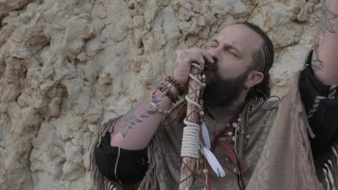 Man dressed as a shaman, standing on a rock in the middle of the desert sands Stock Footage 248671835