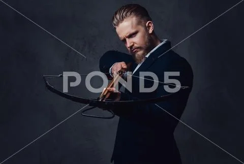 A man dressed in a suit holds crossbow. Stock Photos