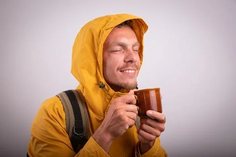 A man dressed in a waterproof jacket drinks a hot herbal tea in a cup. Man .. Stock Photos
