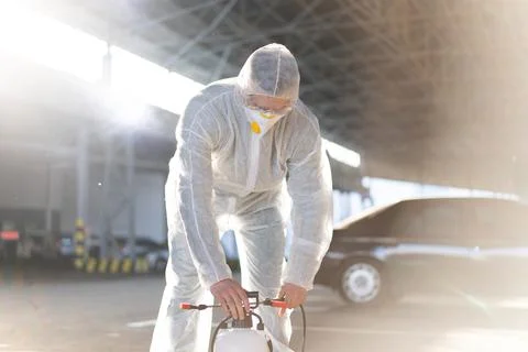 Man dressed white protective overalls spraying surface antibacterial sanitize Foto stock