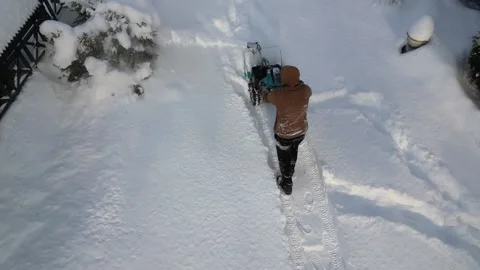 Man dressed in winter clothes moves snow blower forward to clear walkway in park Stock-Footage 327615630