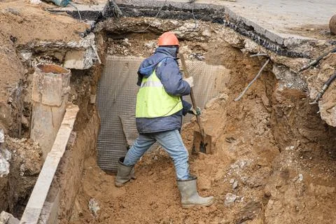 Man dressed as a worker and wearing a construction helmet is digging a large  Stock Photos