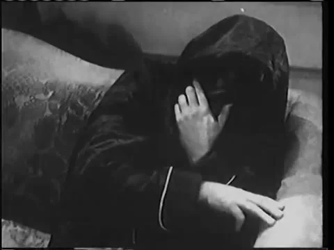 Man in dressing gown with covered head cowering on sofa, 1940s Stock Footage 58858867