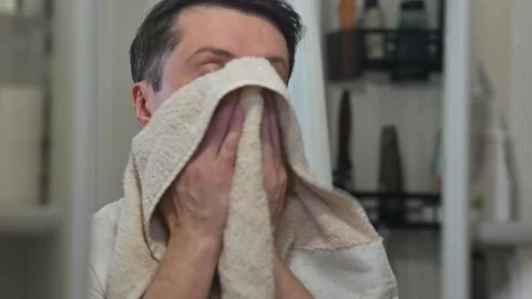 A man dries his face with a towel and styles his mustache in an indoor space. 库存影片 337111624