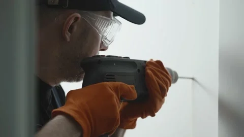A man with a drill in his hands drills a hole in a white wall for mounting Stock-Footage 229100040