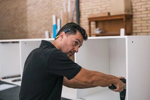 Man drilling a cabinet while looking away distracted in a workshop Stock Photos